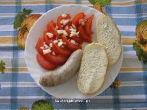 Kiełbasa biała gotowana z pomidorami i czosnkiem na talerzu.