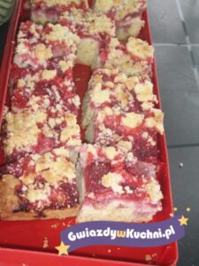 Placek śliwkowy z kruszonką na czerwonym tle, apetyczny i kolorowy.