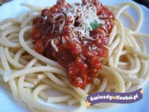 Spaghetti z sosem pomidorowym i startym serem na talerzu.