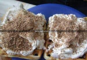 Delikatne gofry z bitą śmietaną i posypką na niebieskim talerzu.