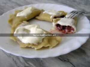 Pierogi z truskawkami z bitą śmietaną na białym talerzu.
