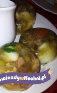Galareta drobiowa z warzywami i przyprawami na talerzu.