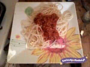 Spaghetti z sosem pomidorowym na kwadratowym talerzu z kwiatowym wzorem.