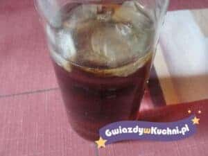 Szklanka domowego ice tea z lodem na czerwonym stole.