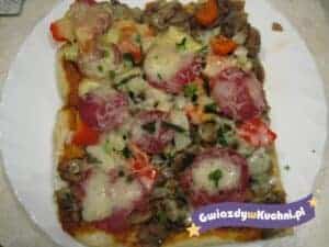 Szybka pizza z kiełbasą, warzywami i roztopionym serem na talerzu.